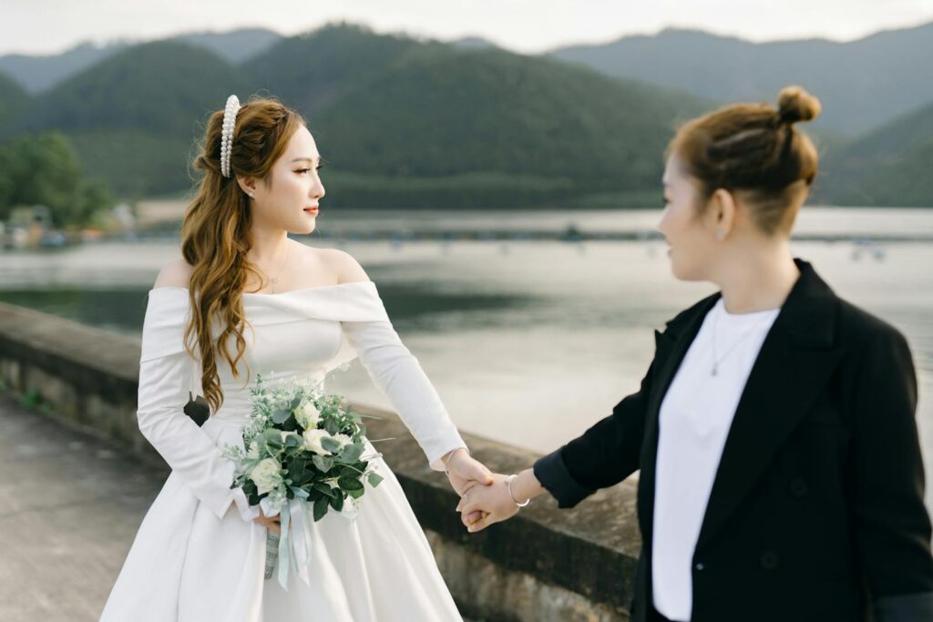 Romantic outdoor wedding of an LGBTQ+ couple by a serene lake with mountains.